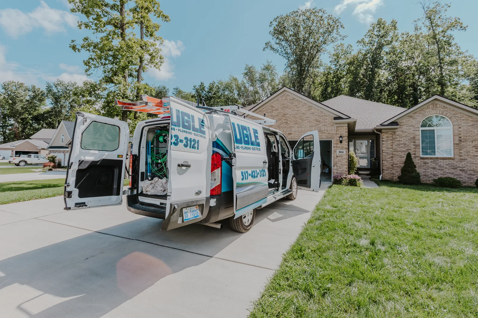 Naugle service van with rear doors open at a customer's driveway during a service call